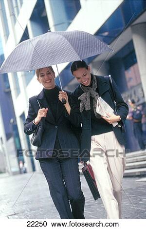 Two women walking under an umbrella in the street View Large Photo Image Stock Image - Two women walking under an umbrella in the street. Fotosearch