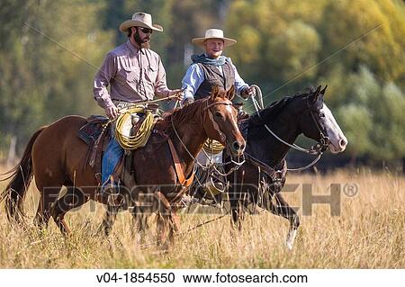 Stock Image - Two wranglers cowboys on horse, Montana, USA. Fotosearch