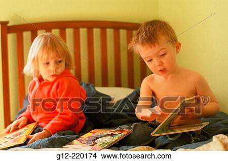 Two year old boy gestures to two year old girl on bed while reading childrens books View Large Photo Image Picture - Two year old boy gestures to two year old girl on bed while reading childrens books. Fotosearch