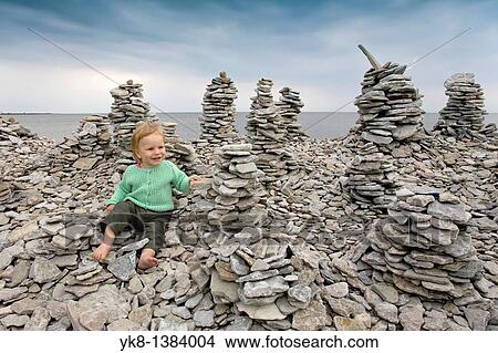 Picture - Two Years Old Kid Girl Buidling Stone Tower on Saaremaa Stony Coast, Saare County, Estonia. Fotosearch