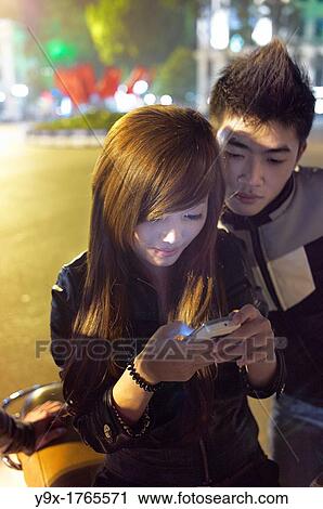 Two young adults look at their cell phone at night on the streets of Vietnam View Large Photo Image Stock Image - Two young adults look at their cell phone at night on the streets of Vietnam. Fotosearch