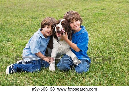 Stock Photo - Two young boys pose with a dog on a grass lawn.. Fotosearch