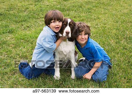 Two young boys pose with a dog on a grass lawn. View Large Photo Image Stock Photo - Two young boys pose with a dog on a grass lawn.. Fotosearch