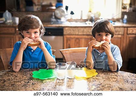 Two young boys sitting in the kitchen eating sandwiches with milk. View Large Photo Image Stock Image - Two young boys sitting in the kitchen eating sandwiches with milk.. Fotosearch