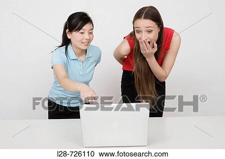 Two young businesswomen using laptop at desk View Large Photo Image Stock Image - Two young businesswomen using laptop at desk. Fotosearch