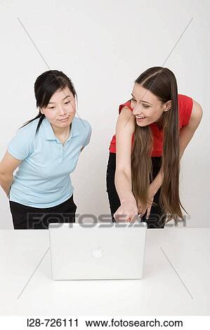 Two young businesswomen using laptop at desk View Large Photo Image Stock Image - Two young businesswomen using laptop at desk. Fotosearch