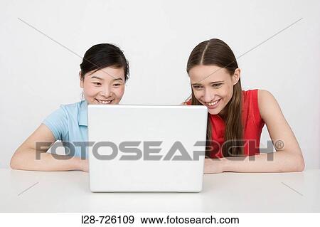 Stock Photo - Two young businesswomen using laptop at desk. Fotosearch