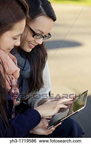 Two young college students enjoying time together with a digital tablet during school break View Large Photo Image Stock Photograph - Two young college students enjoying time together with a digital tablet during school break. Fotosearch