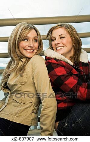 Two young friends sit back to back turning their heads and smiling at each other View Large Photo Image Stock Photo - Two young friends sit back to back turning their heads and smiling at each other. Fotosearch