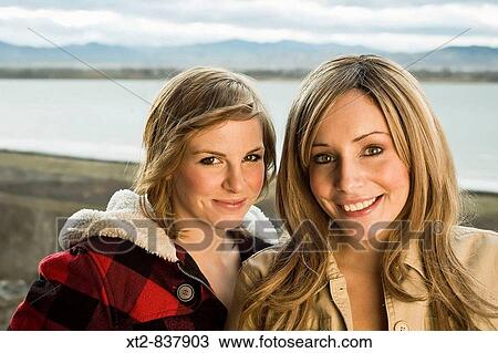 Stock Image - Two young friends stand next to each other in front of a frozen lake and the Rocky Mountains in Colorado, USA. Fotosearch