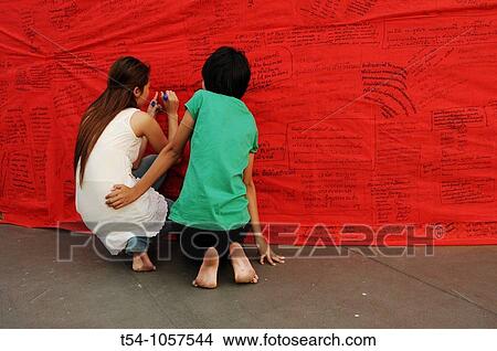 Picture - Two young Friends whriting good wishes on a Red Band at golden Mount Temple in Bangkok. Fotosearch