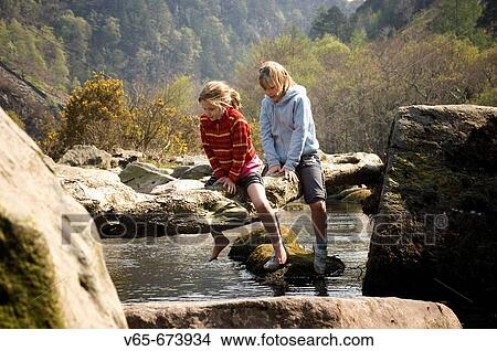 Two young girls, sisters, crawling across a wooden branch on the Glaslyn river near Beddgelert, Snowdonia national park spring afternoon. Wales UK View Large Photo Image Picture - Two young girls, sisters, crawling across a wooden branch on the Glaslyn river near Beddgelert, Snowdonia national park spring afternoon. Wales UK. Fotosearch