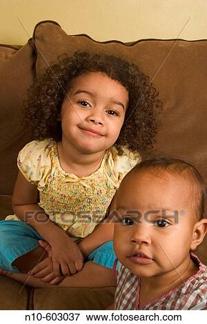 Two young Hispanic/Italian sisters sitting on/standing near a sofa. View Large Photo Image Stock Photo - Two young Hispanic/Italian sisters sitting on/standing near a sofa.. Fotosearch