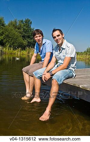 Stock Image - Two young men sitting on a boardwalk at a lake, Germany, Europe. Fotosearch