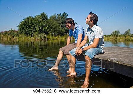 Two young men sitting on a footbridge at a lake View Large Photo Image Stock Photo - Two young men sitting on a footbridge at a lake. Fotosearch