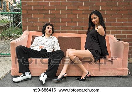 Stock Photograph - Two young party people pose on an old sofa in the street. Fotosearch