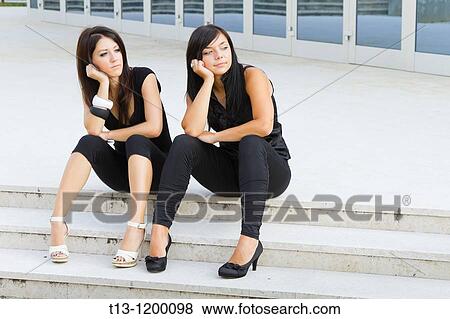 Two young women are sitting on the street and both support their heads with a single hand View Large Photo Image Stock Photo - Two young women are sitting on the street and both support their heads with a single hand. Fotosearch