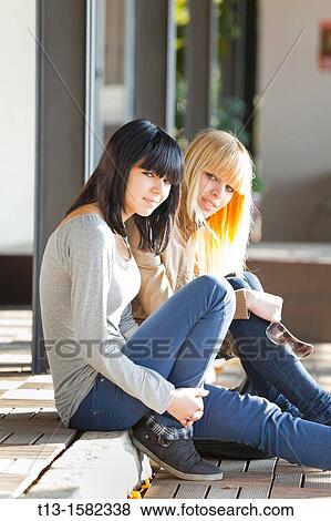 Two young women are sitting on the pavement edge View Large Photo Image Stock Photo - Two young women are sitting on the pavement edge. Fotosearch