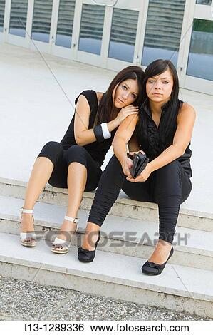 Two young women are sitting on the street View Large Photo Image Stock Photograph - Two young women are sitting on the street. Fotosearch