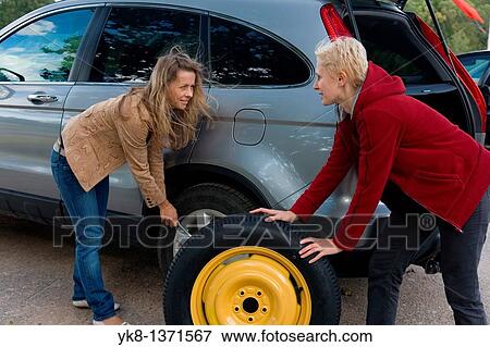 Two young women changing flat spare car tire View Large Photo Image Stock Photo - Two young women changing flat spare car tire. Fotosearch