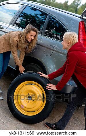 Two young women changing flat spare car tire View Large Photo Image Stock Photograph - Two young women changing flat spare car tire. Fotosearch