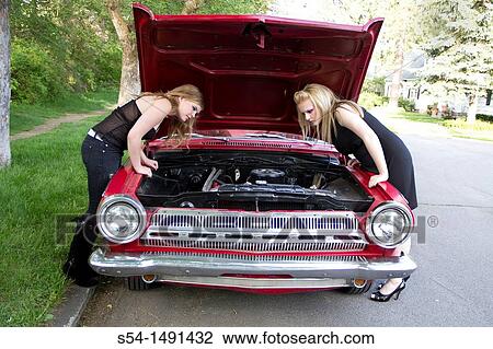 Stock Image - Two young women in 1980s themed makeup with a 1964 Dodge Dart, looking under the hood. Fotosearch