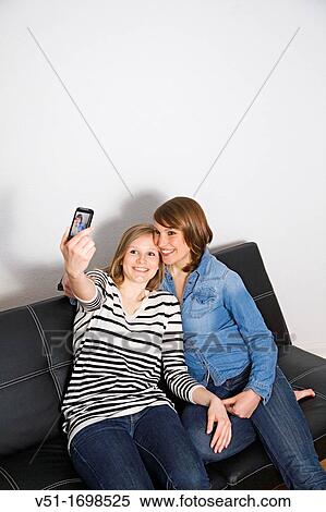 Two young women photographing themselves sitting on sofa View Large Photo Image Stock Photography - Two young women photographing themselves sitting on sofa. Fotosearch