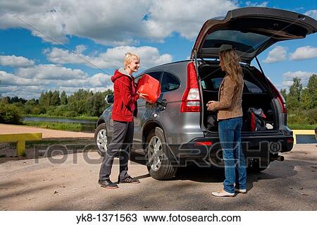 Stock Image - two young women refilling a car tank from canister on road trip. Fotosearch