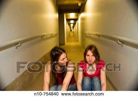 Two young women sitting on the floor in the basement hallway of an office building. View Large Photo Image Stock Image - Two young women sitting on the floor in the basement hallway of an office building.. Fotosearch