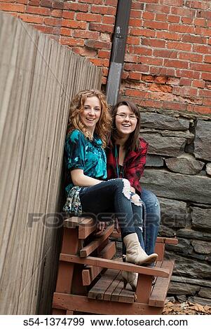 Stock Photo - Two young women sitting outdoors together and laughing. Fotosearch