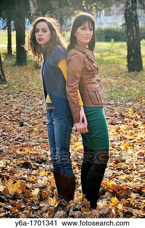 Stock Image - Two young women standing outdoors back to back holding hands. Fotosearch