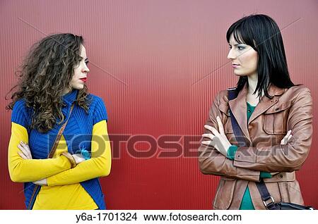 Picture - Two young women standing outdoors looking at each other. Fotosearch