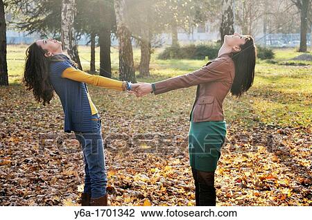 Two young women standing outdoors holding hands View Large Photo Image Stock Image - Two young women standing outdoors holding hands. Fotosearch