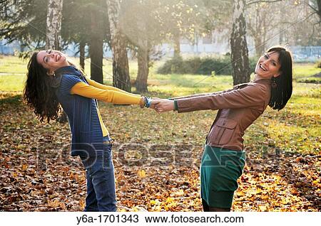 Stock Image - Two young women standing outdoors holding hands. Fotosearch