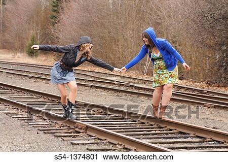 Stock Image - Two young women walking together on railroad tracks. Fotosearch