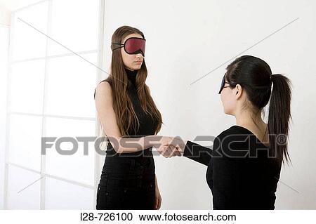 Stock Image - two young women wearing eye mask and shaking hands. Fotosearch