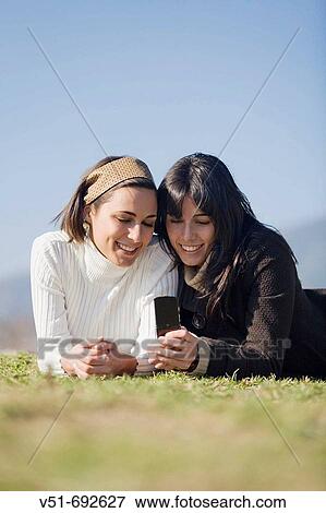 Two young women with mobile in the park View Large Photo Image Stock Photo - Two young women with mobile in the park. Fotosearch