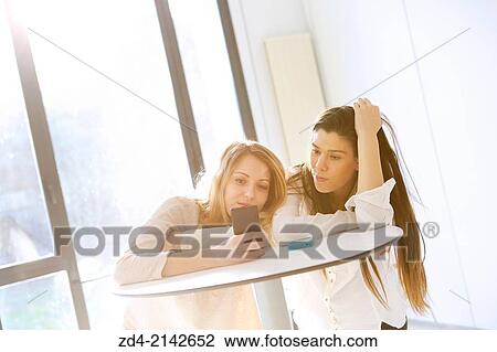 Stock Image - Two young women with smartphones. Fotosearch