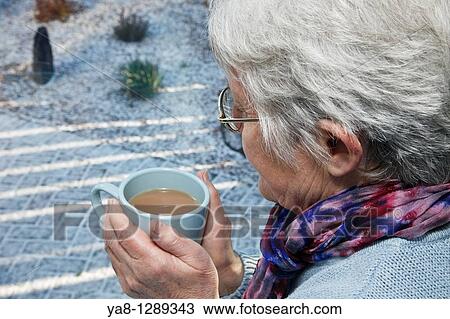 UK, Europe Senior woman holding a warm drink looking out of the window on a cold snowy day in winter View Large Photo Image Stock Image - UK, Europe Senior woman holding a warm drink looking out of the window on a cold snowy day in winter. Fotosearch