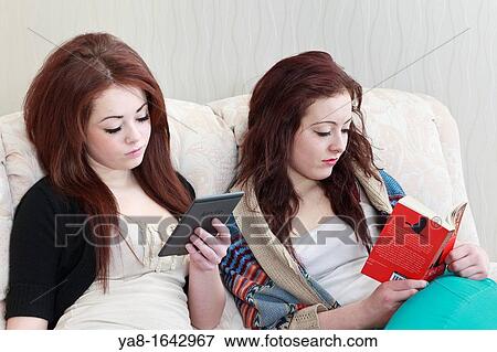 UK Great Britain Europe Two teenage twin girls aged 15 years one reading a Kindle and the other reading a paperback book whilst sitting on a sofa together View Large Photo Image Stock Photo - UK Great Britain Europe Two teenage twin girls aged 15 years one reading a Kindle and the other reading a paperback book whilst sitting on a sofa together. Fotosearch