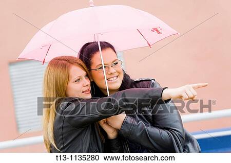 Stock Image - Under pink umbrella young girlfriends. Fotosearch