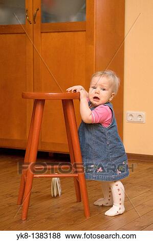 Unhappy Crying Eight Month Old Infant Girl Standing by Stool Chair View Large Photo Image Stock Photo - Unhappy Crying Eight Month Old Infant Girl Standing by Stool Chair. Fotosearch