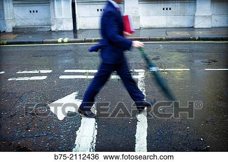unrecognizable executive man, with a folder under his arm and an umbrella walking down the street in the opposite direction of an arrow painted on the asphalt. City of London, England, UK, Europe. View Large Photo Image Stock Photograph - unrecognizable executive man, with a folder under his arm and an umbrella walking down the street in the opposite direction of an arrow painted on the asphalt. City of London, England, UK, Europe.. Fotosearch
