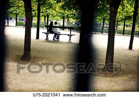 Unrecognizable young couple sitting on a bench in the gardens of the Palais Royale, Paris, France View Large Photo Image Stock Image - Unrecognizable young couple sitting on a bench in the gardens of the Palais Royale, Paris, France. Fotosearch