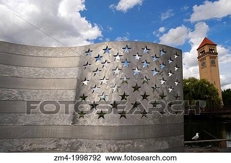 Stock Image - USA, WASHINGTON STATE, SPOKANE, RIVERFRONT PARK, ALUMINUM BENCH (AMERICAN FLAG) ART, CLOCK TOWER IN BACKGROUND.. Fotosearch