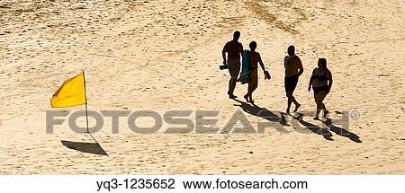 Stock Image - Vacationers walking by a yellow flag. Orion Beach, Castro Urdiales, Cantabria, Spain.. Fotosearch
