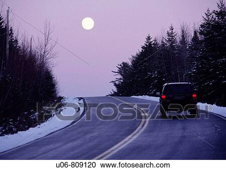 Stock Image - vehicle on a highway at twilight with the moon rising in the winter. Fotosearch