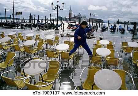 Stock Photo - Venice Italy A girl jumps between cafe chairs to avoid getting wet during a high tide, acqua alta, on the Piazzetta, San Marco. Fotosearch