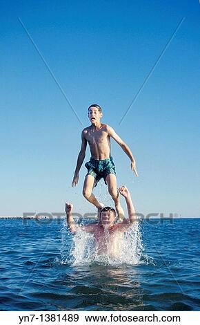 vertical image of two teenage boys fooling around at the beach with one tossing the other into the air above the water View Large Photo Image Stock Photo - vertical image of two teenage boys fooling around at the beach with one tossing the other into the air above the water. Fotosearch