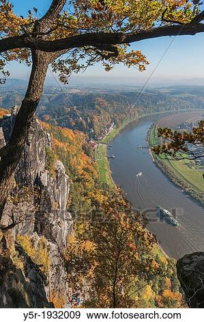 Stock Photo - View from the spectacular rock formation Bastei (Bastion) to health resort Rathen and the Elbe River.. Fotosearch